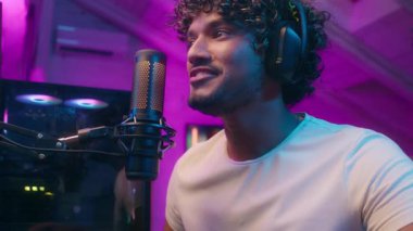 Hintli Müslüman Arap adam mikrofonla konuşuyor kameraya bakıyor gülümsüyor flaşçı erkek oyuncu bilgisayar siber sporu yapıyor çevrimiçi oyun blogcu kulaklıklar neon ışık bağımlısı