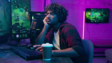 Uykulu, sıkılmış Arap, Hintli, video oyunu oynayan, siber sporcu, oyun oynayan, tembel, kahve içen, yorgun, erkek, e-spor, bilgisayar bağımlısı, ev bağımlısı, uykusuzluğu çeken, uykulu, can sıkıntısı çeken bir adam.