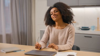 Afrika kökenli Amerikalı genç kız milenyum kızı. Kadın iş kadını. Gözlüklerini çıkarıyor, mutfakta bilgisayar çalışıyor.