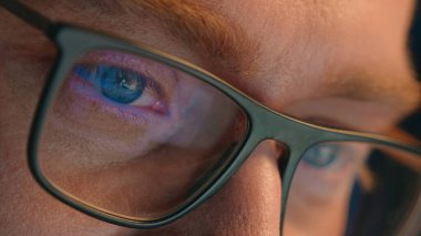 Close up cropped view details male eyes in eyeglasses eyewear glasses Caucasian man business guy businessman night gamer programmer looking laptop computer screen online reflection eye health vision