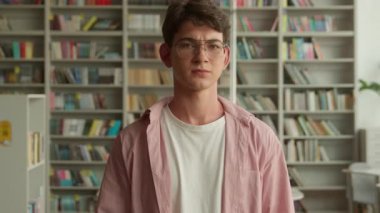 Kütüphane kitapçısında üniversite fakültesi hayal kırıklığına uğramış Kafkasyalı öğrenci kameraya bakıyor tatminsiz erkek öğrenci erkek öğrenci eğitimi alıyor.