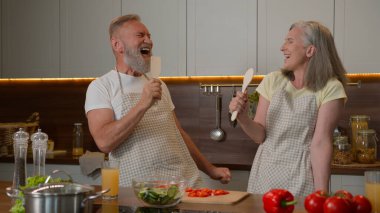 Kafkas aşığı komik bir çift olgun orta yaşlı yaşlı yaşlı eş ve koca emekli olmuş evli aile şarkıları söyleyip kaşık mutfak eşyaları neşeli gülen kadın mutfakta sağlıklı yemekler pişiren mutlu bir adam.