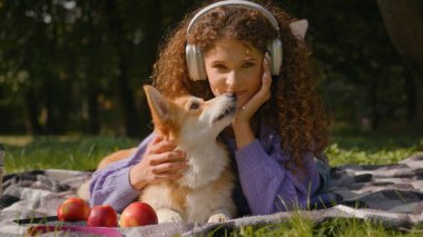 Beyaz, mutlu, kıvırcık saçlı kız. Kulaklıkla müzik dinliyor. Yaz pikniğinde dinleniyor.