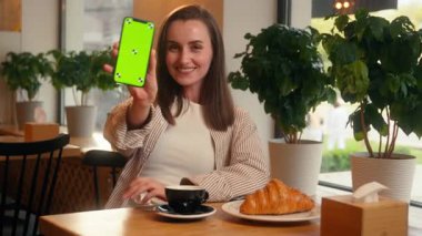 Gülümseyen mutlu kadın kafe ziyaretçi müşterisi kafeterya restoranında elinde cep telefonu, elinde yeşil ekran akıllı telefon görüntüsü, krom ekran menü siparişi gibi kameraya gülümse.