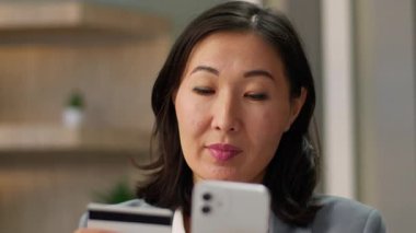 Asyalı kadın alışverişçi tüketici mutlu tüketici kadın Çinli Çinli Japon iş kadını memnun iş kadını ofis telefonundan internet üzerinden alışveriş yapıyor internet banka kredi kartı parası