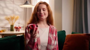 Evde gülümseyen beyaz bir kadın portresi oturma odasında elinde kırmızı elma meyvesi kokan genç kız kameraya bakıyor güzel kokular alıyor diyet sağlıklı beslenme, ekolojik dağıtım.