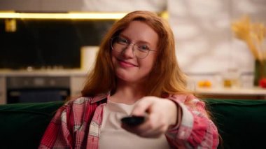 Mutlu gülümseyen duygusal asık suratlı beyaz kadın hafta sonu gevşemiş genç kız. Rahat bir evde patlamış mısır tutuyor. TV 'yi açıyor, televizyon izliyor, film serisini seçiyor.