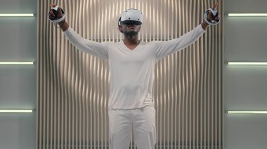 Fütürizm oyun keşfi siber uzay 3D simülasyon internet video oyunu sanal gerçeklik VR gözlüklü Afrikalı Amerikalı erkek adam beyaz fütüristik odada oynuyor modern teknoloji çevrimiçi metaevren