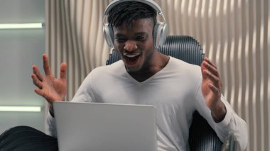 Beyaz fütürizm stüdyosundaki Afro-Amerikan etnik siber adam kapalı mekanda iş adamı erkek kullanıcı hacker iş adamı kulaklıklarda fütüristik adam dizüstü bilgisayar başarısı Bilgisayarda harika haberler elde