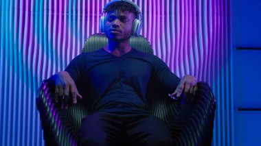 Afrikalı Amerikalı erkek, koltukta oturup dinleniyor. Huzur içinde dinleniyor. DJ, modern kablosuz kulaklıklarda müzik dinliyor.