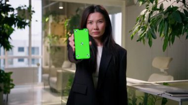 Asyalı üzgün Çinli iş kadını Koreli iş kadını alıcı ofiste cep telefonu yeşil ekran krom anahtar boş fotokopi uzayı akıllı telefon uygulaması online alışveriş reklamları tutuyor.