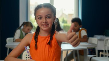 Mutlu öğrenci portresi küçük kız öğrenci kız öğrenci kız öğrenci Kafkasyalı kız başparmağıyla gülümsüyor jest eğitimi tavsiye ediyor ödev kitapları yazıyor, okul arkadaşlarını öğreniyor.