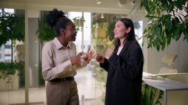 Afro-Amerikalı Asyalı gülümseyen Çinli kadınlar birlikte gülen neşeli kızlar iki iş kadını iş ortağı öğrenci arkadaşlar ofiste sohbet ediyorlar beşlik çakın.