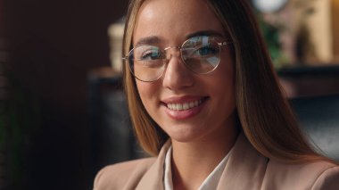 Güzel, kendine güvenen, beyaz, pozitif iş kadını, bayan iş kadını, girişimci, gözlük takan gözlüklü, optometri görünümlü kamerayı takıp ofisin içinde gülümsüyor.