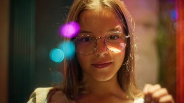 Neşeli, beyaz, Asyalı, küçük bir kız çocuğu bardağa elle dokunuyor. Şehirli, neon ışıklı, umut verici ergen kız çocuğu destekliyor.