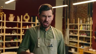 Kızgın, kızgın, kızgın, Kafkasyalı erkek, küçük işletme sahibi, çömlekçi, satıcı, el sanatları işçisi, işaret parmağıyla kamera hareketine bakıyor. Öfkelisin, öfkelisin, bağırıyorsun, kapalı dükkanda bağırıyorsun.