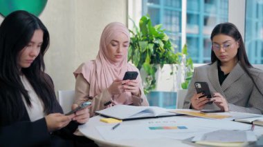Çok ırklı kadın çeşitlilik takımı kızları iş arkadaşları internet üzerinden iş kadınları cep telefonlarını aşırı kullananlar, dikkat dağıtıcı cihazlar, cep telefonu bağımlıları toplantı odasında sosyal medya.