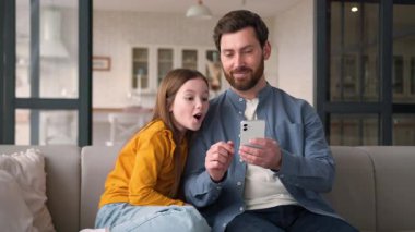 Neşeli, mutlu, beyaz bir aile babası, baba kutlayan bir baba, erkek, kız, cep telefonu başarısını cep telefonuyla kazanan küçük çocuk, zaferi kutlayan bir cep telefonu zaferi.