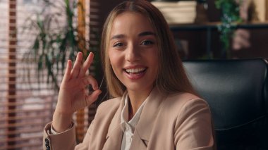 Mutlu gülümseyen Kafkasyalı başarılı iş kadını kız iş kadını neşeli ofis çalışanı bayan kamera tebessümüne bakıyor tamam güzel jest güzel tepki güzel kapalı alanda başarı onaylayın