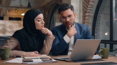 İki iş arkadaşı ofis kafesinde şirket işlerini tartışıyor. Çok ırklı erkek çalışanlar, Hintli erkek Müslüman kadın tesettürlü çeşitli iş kadınları dizüstü bilgisayarlar yazıyor.