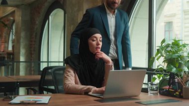 Arap Hintli erkek patron işkadını iş kadını laptopunun ofiste çalışmasına yardım et iki iş arkadaşı bilgisayar projesinde danışmanlık yapıyor tesettürlü stajyer kadına yardım et çok ırklı takım çalışmasına danış