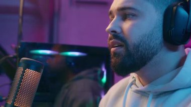 Kafkasyalı erkek oyuncu portresi yakın çekimde video oyunu bağımlısı bilgisayar bağımlısı e-spor siber oyun kulaklıklarıyla gece vakti mikrofonla kapalı mekanda neon ışığı ile oynamak hüsranda kaybedilen başarısızlığı altüst ediyor.