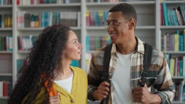 İki mutlu öğrenci Kafkas kadın Afrikalı Amerikalı erkek öğrenci kütüphanede pozitif eğitim üniversiteden arkadaşlar sınıf arkadaşları gülümsüyor lisede gülerek kameraya bakıyor.