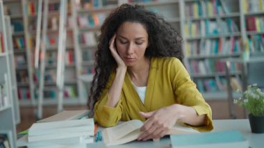 Kafkas asıllı kadın öğrenci kitap okuyor, zor sınavlar hazırlıyor, kütüphanede sıkılıyor, kız öğrenci okuyor, üzgün bir şekilde öğreniyor, lise eğitiminden bitap düşmüş bir sayfa okuyor.