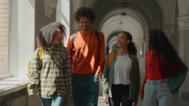 Üniversite koridorunda yürüyen ve gülümseyen dört arkadaşla konuşan bir grup mutlu öğrenci lise koridorunda yürüyen Afrikalı Amerikalı erkek ve Arap İspanyol kadın kızlar sınıfa giriyor.