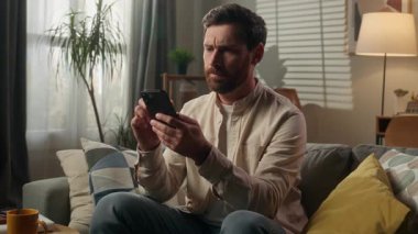 Stresli, sinirli, ev sahibi, ev sahibi iş adamı. Evdeki koltukta cep telefonu kullanıyor. Kafkasyalı, öfkeli, sinirli, kötü mesaj sorunu.