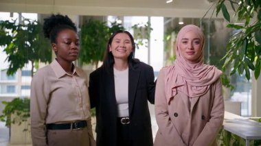 Üç güzel çok ırklı kız etnik çeşitlilik iş arkadaşları iş arkadaşları iş kadınları gülümseyen iş kadınları ofis ortaklığında birlikte poz veren Afrikalı Müslüman Asyalılara bakıyorlar