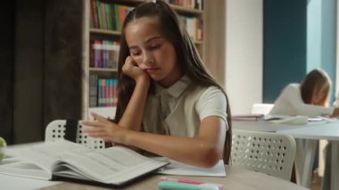 Sıkılmış beyaz kız öğrenci çocuk öğrenci kütüphanede kitap okudu üzgün öğrenci öğrenci hayal kırıklığına uğradı sıkıcı ders çalışmaktan yorgun düştü sınıf eğitiminde uykulu okuma