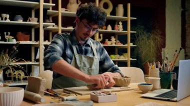 Kafkasyalı erkek, erkek çömlekçi, sanatçı, sanat heykeltraş, el yapımı, masa çömleği atölyesinde laptop video, el sanatları, seramik tasarım hobisi kullanarak merdane modelliği yapıyor.