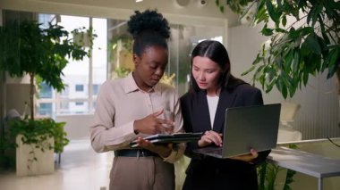 Çeşitli iş ortakları iki çok ırklı kız Afrikalı Amerikalı, Asyalı, Koreli iş arkadaşları iş arkadaşları, gülümseyen yöneticiler ofisteki fikir birliği dizüstü bilgisayar projeleri satışlarını tartıştılar.