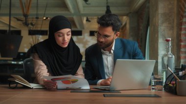 Erkek, kadın, Arap, erkek, kadın, tesettürlü, erkek, erkek, iş kadını, iki mutlu iş arkadaşı, yöneticiler pazarlama grafiklerini analiz eden, dizüstü bilgisayarda yazı yazan iki iş arkadaşı.