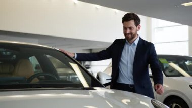Beyaz adam müşteri alıcısı heyecan dolu erkek galerisini inceliyor. Yeni araba taşıma aracına dokunuyor. İş adamı satın alıyor.