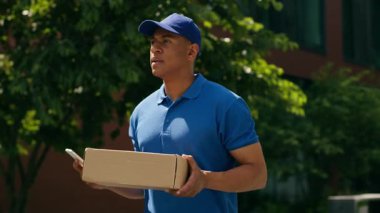 Küçük işletme konsepti Afro-Amerikan kurye cep telefonu uygulaması ile adres arayan şehir teslimatçısı erkek postacı e-ticaret alışveriş siparişi taşıması zor