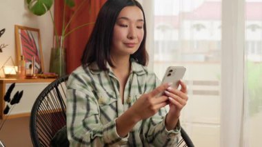 Neşeli Asyalı Koreli Çinli kadın cep telefonu kullanıyor akıllı telefonlu kız gülümsüyor kameraya bakıyor el sallayan kadına olumlu iş kadınını selamlıyor ev hanımı jesti merhaba