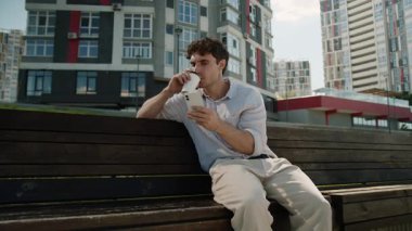 Kafkasyalı bir gencin elinde bir fincan kahve, cep telefonu, akıllı telefon, şehirli şaşkın adam, kötü haber, internetteki kötü haber, kafası karışmış, afallamış iş adamı.