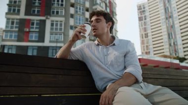 Beyaz Avrupalı bir adam bankta oturmuş kahve molası veriyor. Müşteri siparişi veriyor. Lezzetli içici, işveren öğrenci, işveren, işveren, şehir dışında dinleniyor.
