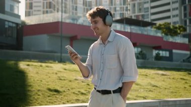 Kulaklıkla müzik dinleyen mutlu Kafkasyalı genç adam enerjik kaygısız şehir çocuğu dans eden şarkı listesi ses kaydı hafta sonu eğlence cep telefonu öğrenci teknolojisi açık hava eğlencesi