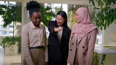 Mutlu gülümseyen çok ırklı iş kadınları Afrikalı Müslüman Asyalı takım kızları iş arkadaşları el ele tutuşan iş kadınları takım çalışması jestleri silah arkadaşlığı birliği destek ortaklığı başarısı ofiste