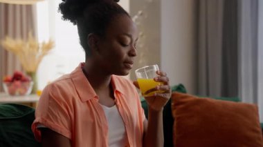 Mutlu, gülümseyen, Afro-Amerikan, iş kadını, ev sahibi, televizyon izleyen, portakal suyu içen, meyve suyu içen, meyve suyu içen, kapalı salonda vitamin kokteyli içen, iş kadını.