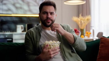 Kafkasyalı, beyaz, erkek, ev sahibi, patlamış mısır yiyor, TV dizisi izliyor, film izliyor, medya televizyon bağımlılığı yayını yapıyor.