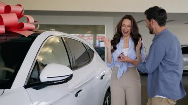Otomobil galerisindeki beyaz çift, araba galerisindeki adam, erkek arkadaş, koca, hediye paketi, yeni arabadan, güzel bayan, kadın, kız, kadın, kadın, kız arkadaş, araba ailesine sarılan kadın.