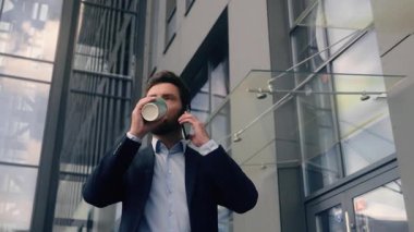 Ofis binasının yanında yürüyen girişimci işe gidiyor, konuşuyor, cep telefonu konuşuyor, akıllı telefon konuşuyor, içiyor, kahve içiyor, Kafkasyalı erkek işadamı, şehirde erkek işadamı işi yapıyor.