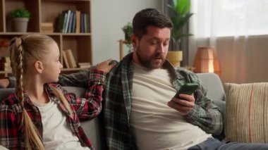 Mutlu, beyaz, cep telefonu kullanan bir adam, cep telefonu kullanan bir kızın dikkatini dağıtan küçük bir okul kızının dikkatini dağıtıyor. Pembe taç takan bir baba, komik bir baba.