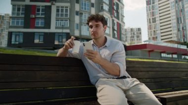 Kafası karışmış Kafası karışık beyaz adam cep telefonu kullanıyor. Akıllı telefon kullanıyor. Haber okuyan erkek öğrenci, kahve içiyor.