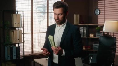 Kafkasyalı başarılı orta yaşlı iş adamı elinde yığınla para tutuyor iş adamı dolarları sayıyor iş adamı işveren para sayan girişimci ofiste kameraman erkeğe bakıyor