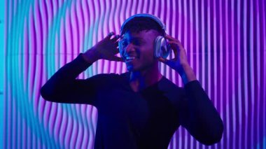 Mutlu bir gülümseme özgürce dans eden Afrikalı Amerikalı adam kulaklıkla karışık müzik dinliyor aktif bir gülümseme dansı yapıyor koyu mavi fütürizm uzay erkeği fütüristik konseptinde müzik dinliyor